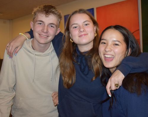 Tre efterskoleelever står i spisesalen på Sædding Efterskole og har armen rundt om hinanden, mens de smiler til kameraet