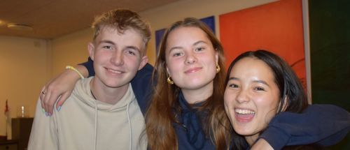 Tre efterskoleelever står en aften med armene rundt om hinanden i spisesalen på Sædding Efterskole. De smiler