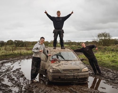 Efterskoleelever står ved markræs bil på en mudret mark
