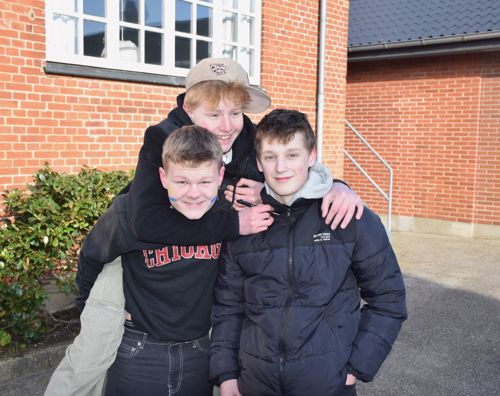 3 efterskoledrenge står i gården på Sædding Efterskole – smilende og den ene sidder på de andres ryg. 