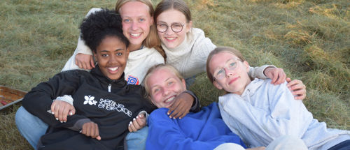 Viceleder søges til Sædding Efterskole. Her ses fem piger fra Sædding Efterskole, som ligger sammen i græsset og smiler til kameraet.