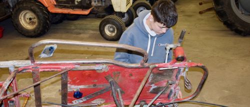 Efterskoledreng sidder på gulvet i værkstedet på Sædding Efterskole og er ved at reparere et køretøj.