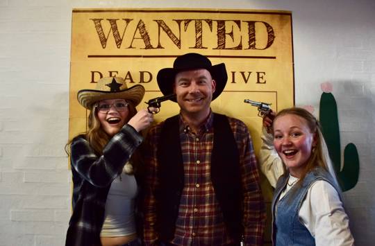 Forårsfesten på Sædding Efterskole er en temafest. Her var temaet Cowboyfest. Et par elever står foran billedvæggen, hvor de peger et par skydere mod en lærer.