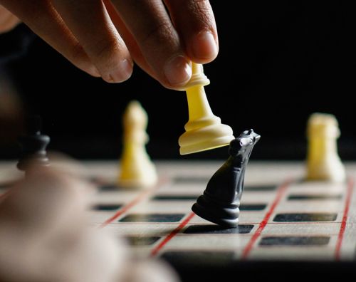 Skak Valgfag Sædding Efterskole | En hånd løfter en hvid bonde og slår en sort hest ud i spillet skak.