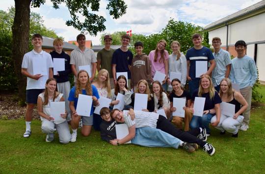 9.kl. på Sædding Efterskole med deres eksamenspapirer. De står på plænen foran hallen og smiler alle sammen 