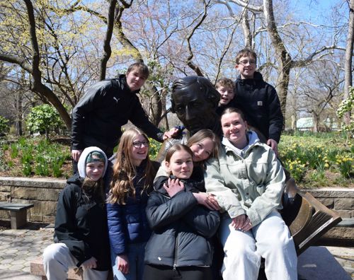 En flok piger fra Sædding Efterskole sidder ved en statue af H.C. Andersen i Central Park, New York