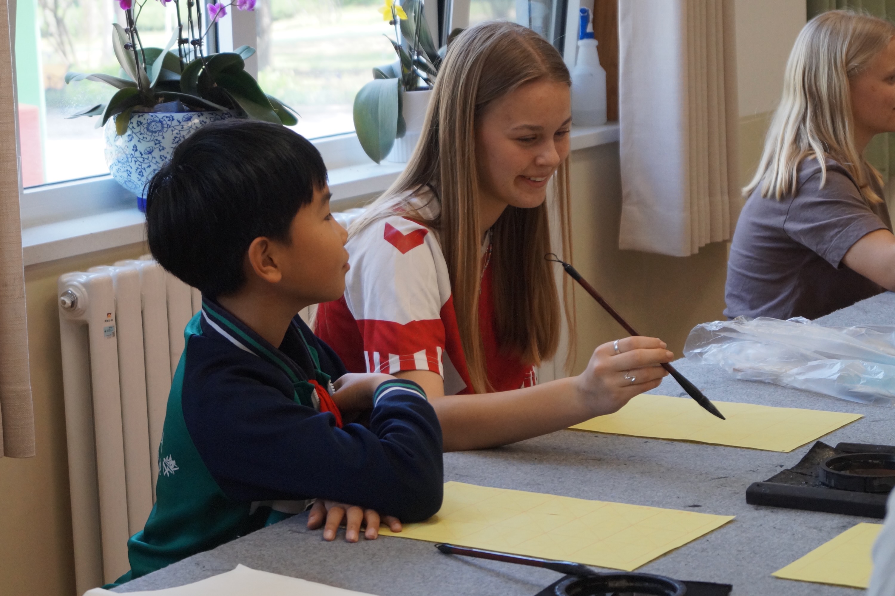 En elev fra Sædding Efterskole lærer at tegne kinesiske tegn af en skoleelev i Kina