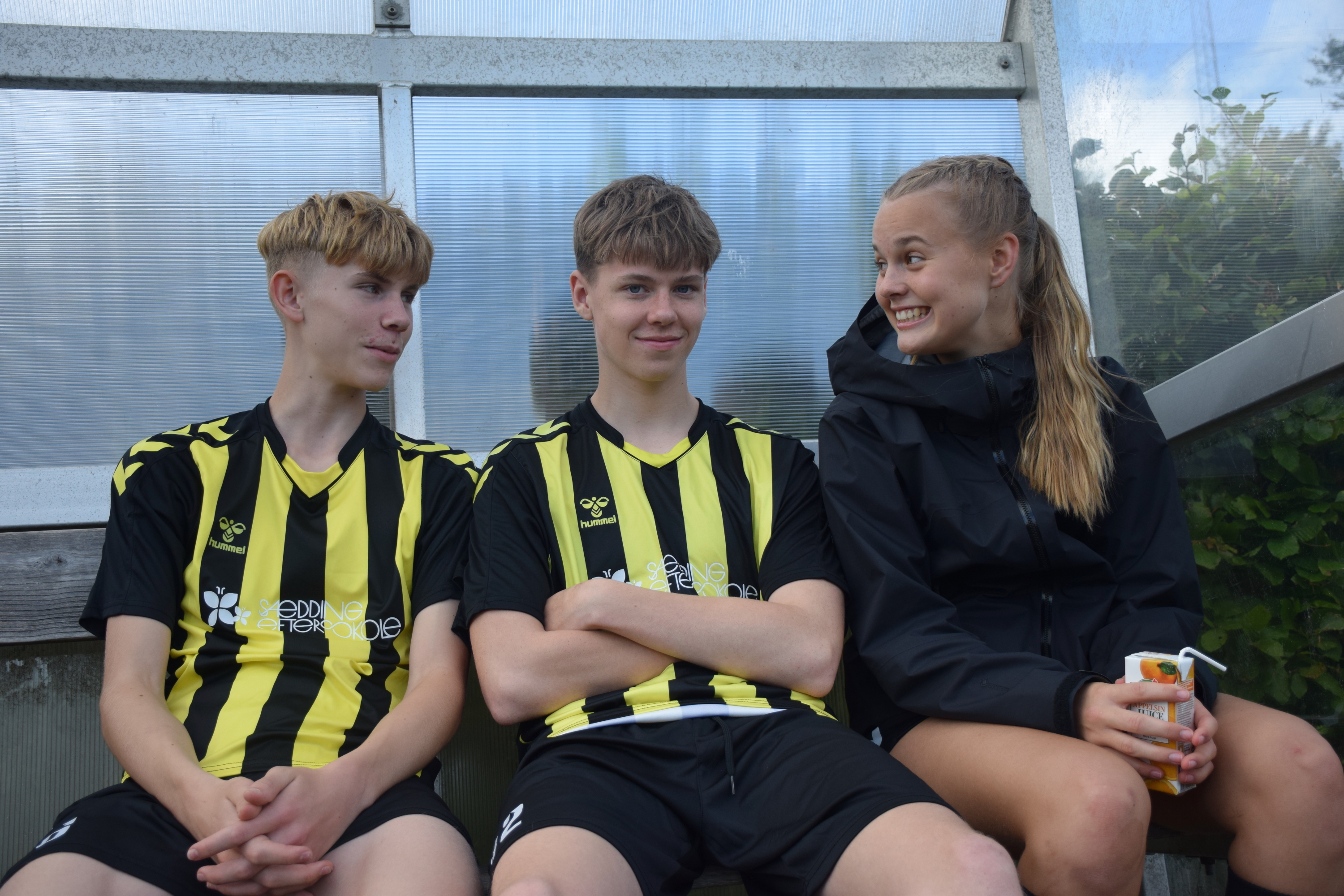 Sportsstævne Sædding Efterskole | To efterskoledrenge sidder og venter på kamp, mens en efterskolepige sidder ved siden af og smiler. 