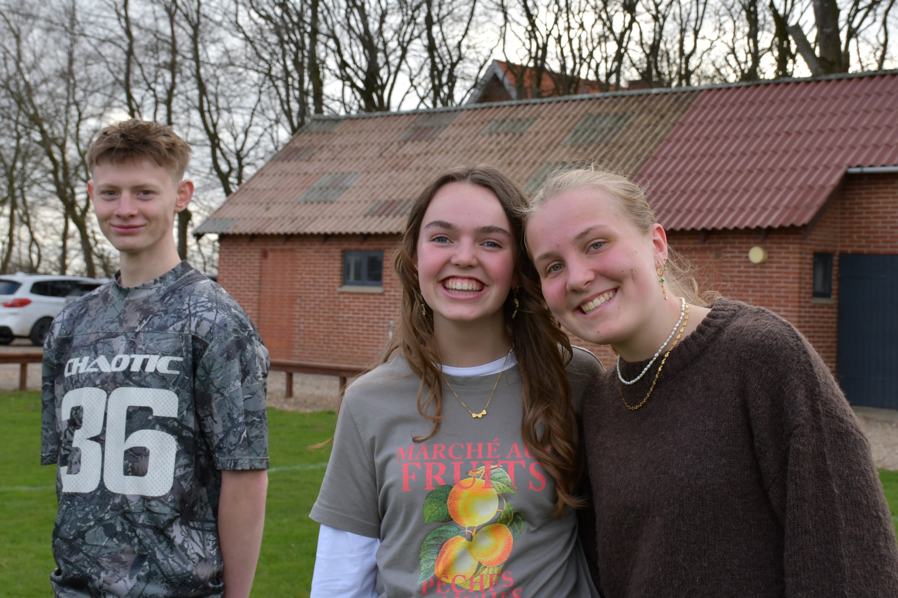 Tre efterskoleelever står på efterskolens fodboldbane og smiler til kameraet. 