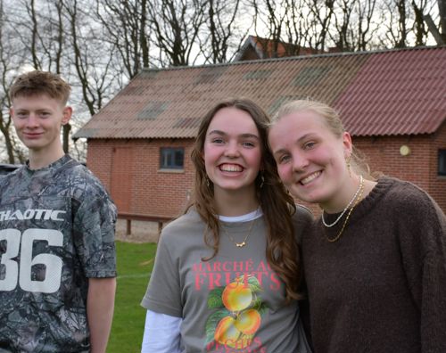 Tre efterskoleelever står på efterskolens fodboldbane og smiler til kameraet.