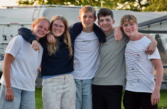 En flok glade efterskoleelever står med armene rundt om hinanden - smilende på afslutningsturen på Mørkholt Camping.