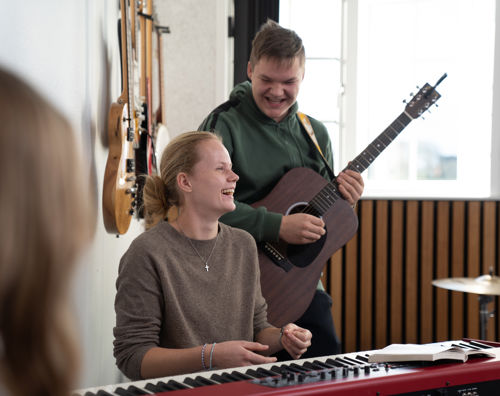 Efterskolernes dag. To elever spiller i efterskolens musiklokale. Pigen sidder ved klaveret, mens en dreng spiller guitar bagved. De griner begge to.