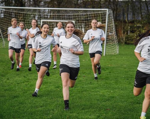 Sædding Efterskoles pigehold i fodbold løber på græsbanen til træning. 