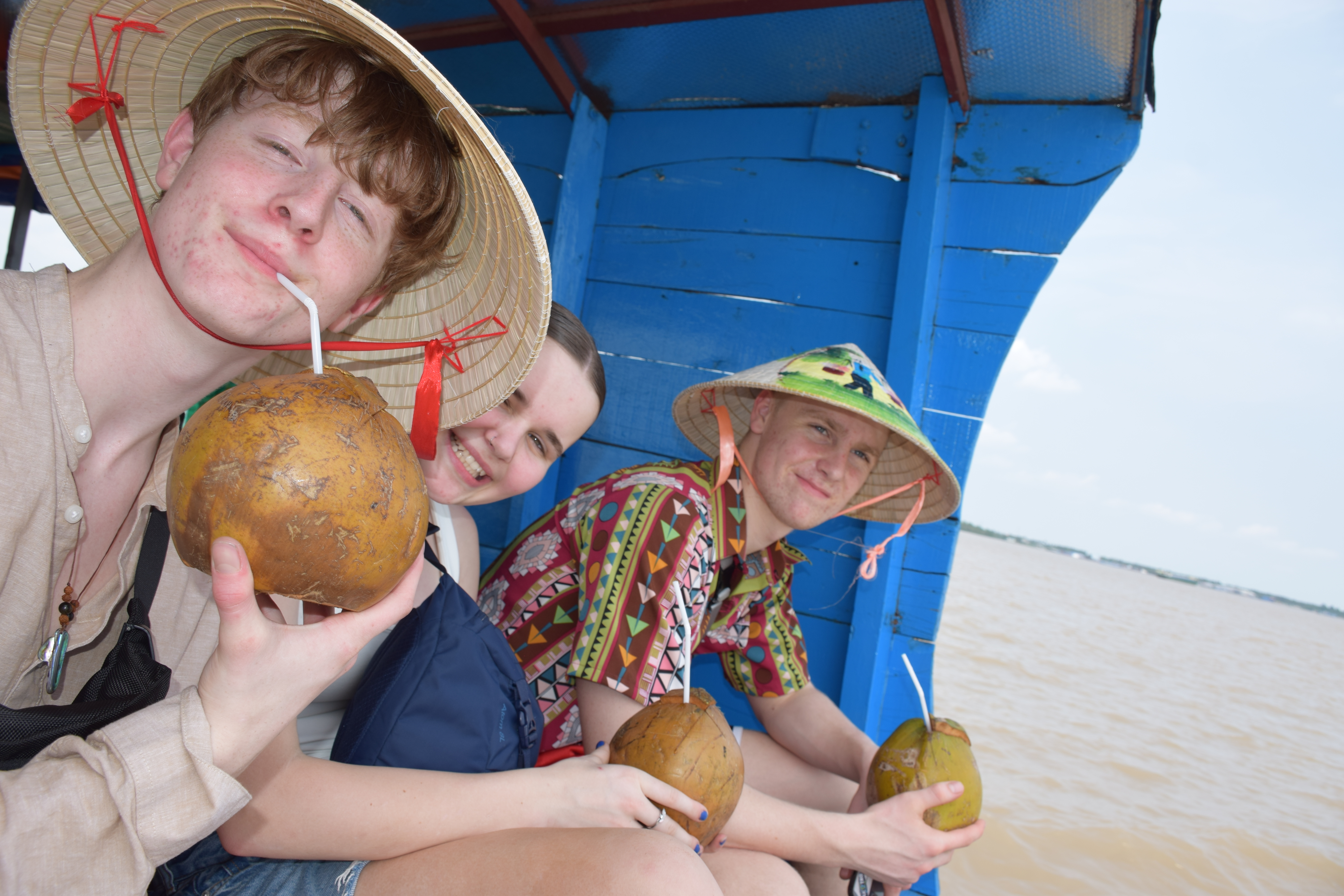 Tre elever fra Sædding Efterskole drikker drinks af en kokosnød, mens de sidder på en båd i Vietnam