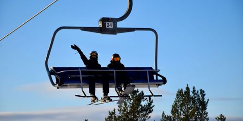 To elever sidder i lift på skitur med Sædding Efterskole. Den ene vinker. 