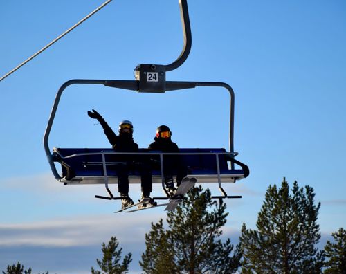 To elever sidder i lift på skitur med Sædding Efterskole. Den ene vinker.