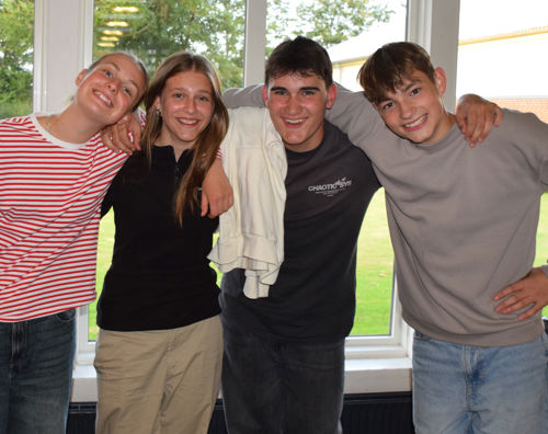 En flok glade efterskoleelever fra Sædding Efterskole, står med armene rundt om hinanden og smiler til kameraet.