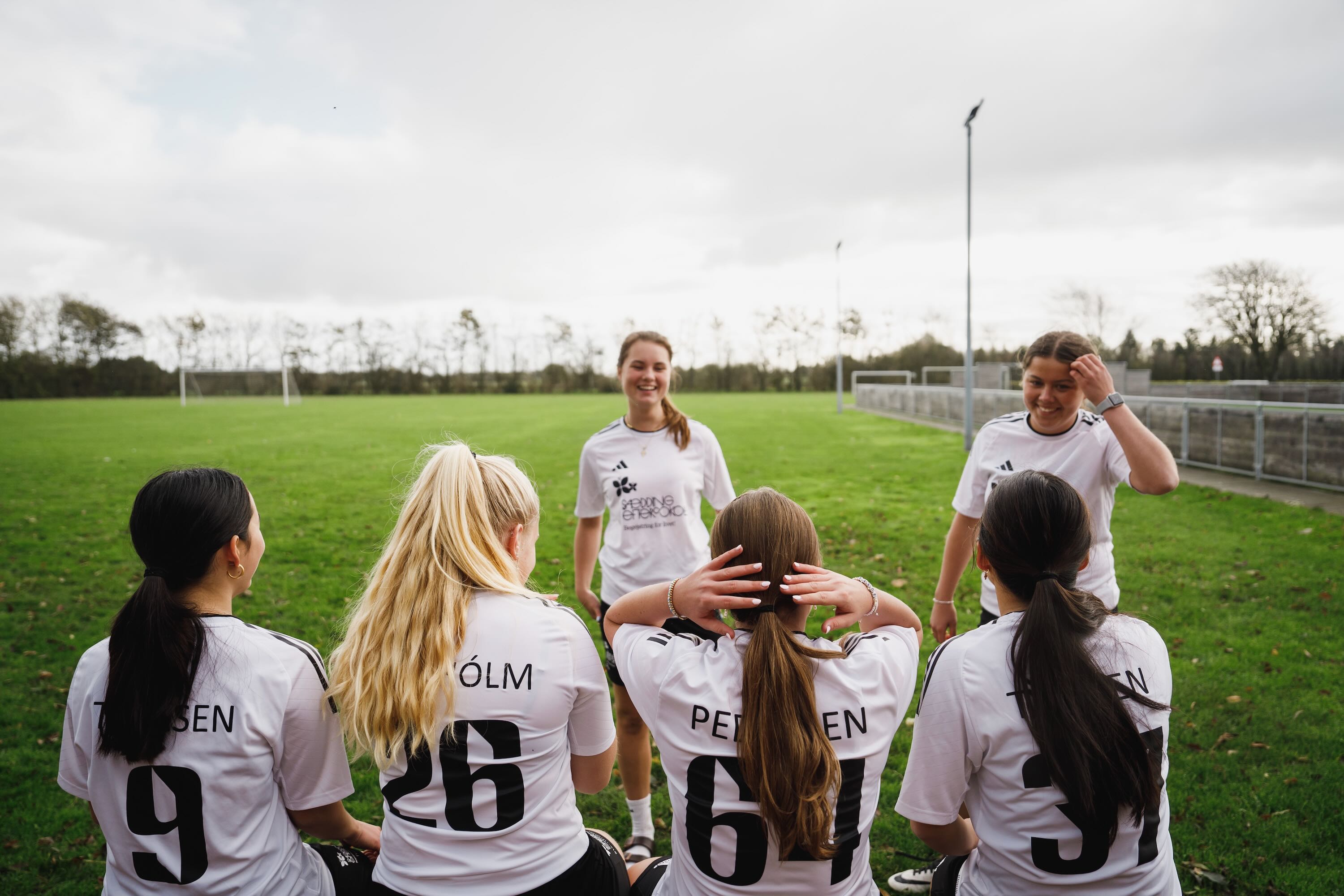Linjefaget Sport | En flok efterskolepiger sidder klar til at spille fodbold ved fodboldbanen.