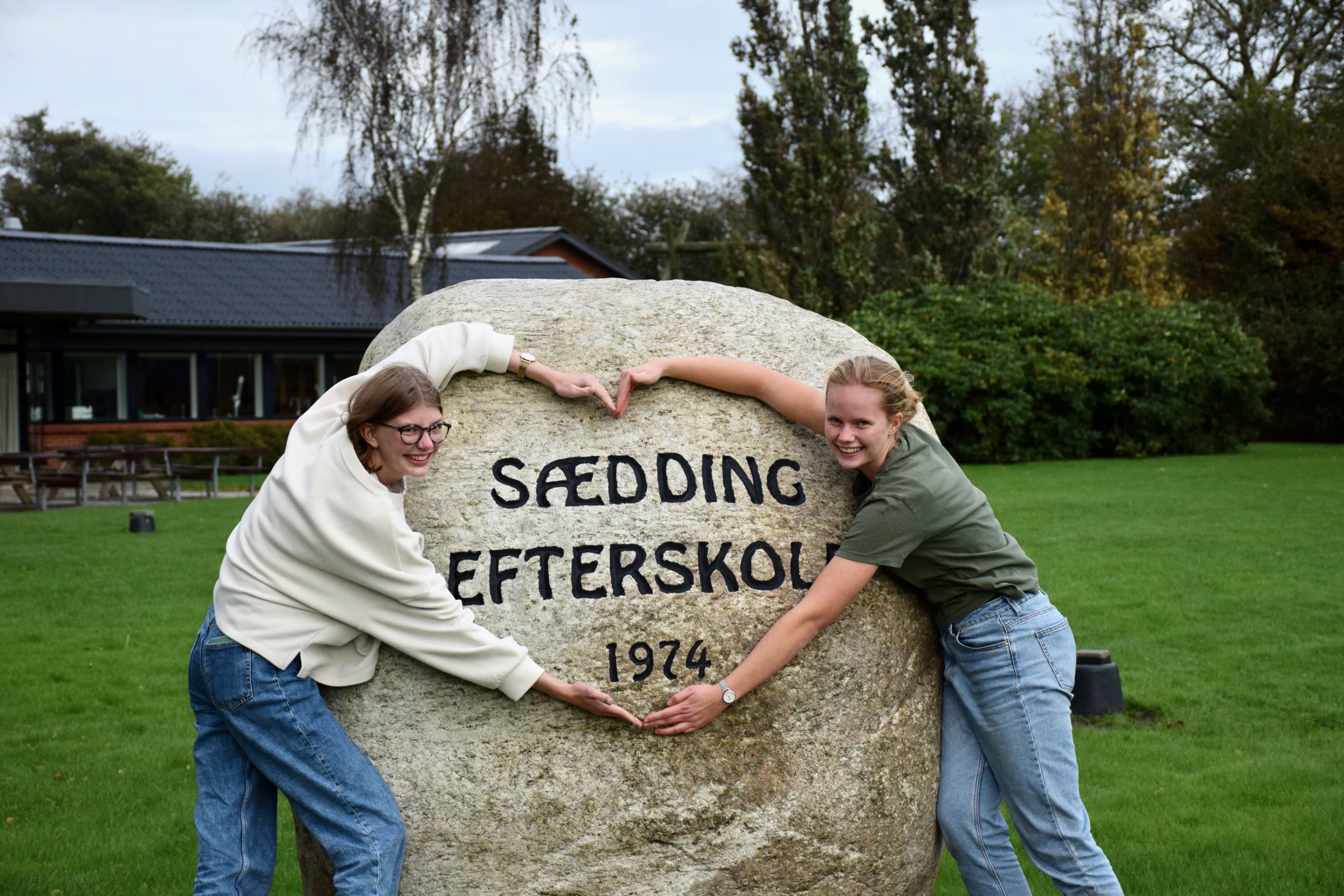 To efterskolepiger fra Sædding Efterskole, danner et hjerte med deres arme om stenen, hvorpå der står 1974