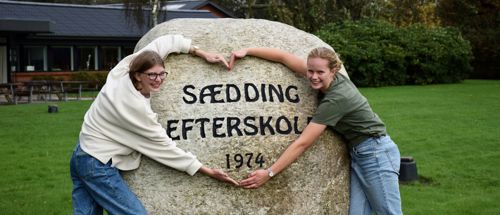 To efterskolepiger fra Sædding Efterskole, danner et hjerte med deres arme om stenen, hvorpå der står 1974