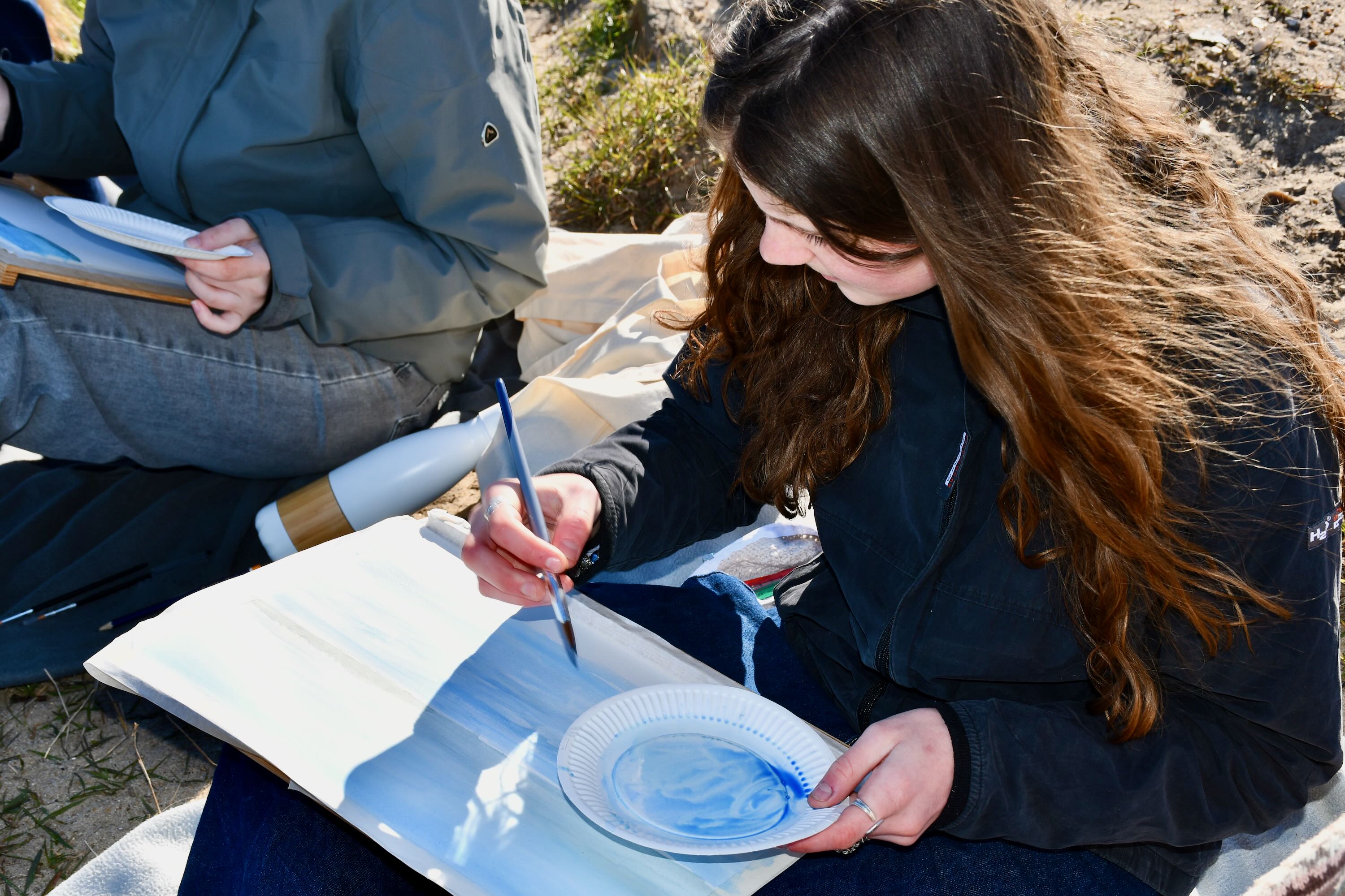 Kunst og Design Sædding Efterskole | En pige sidder på en strand og maler akvaral med linjefaget Kunst og Design 
