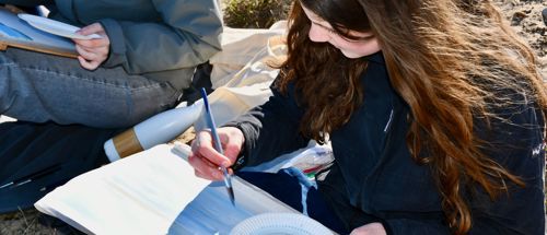 Kunst og Design Sædding Efterskole | En pige sidder på en strand og maler akvaral med linjefaget Kunst og Design