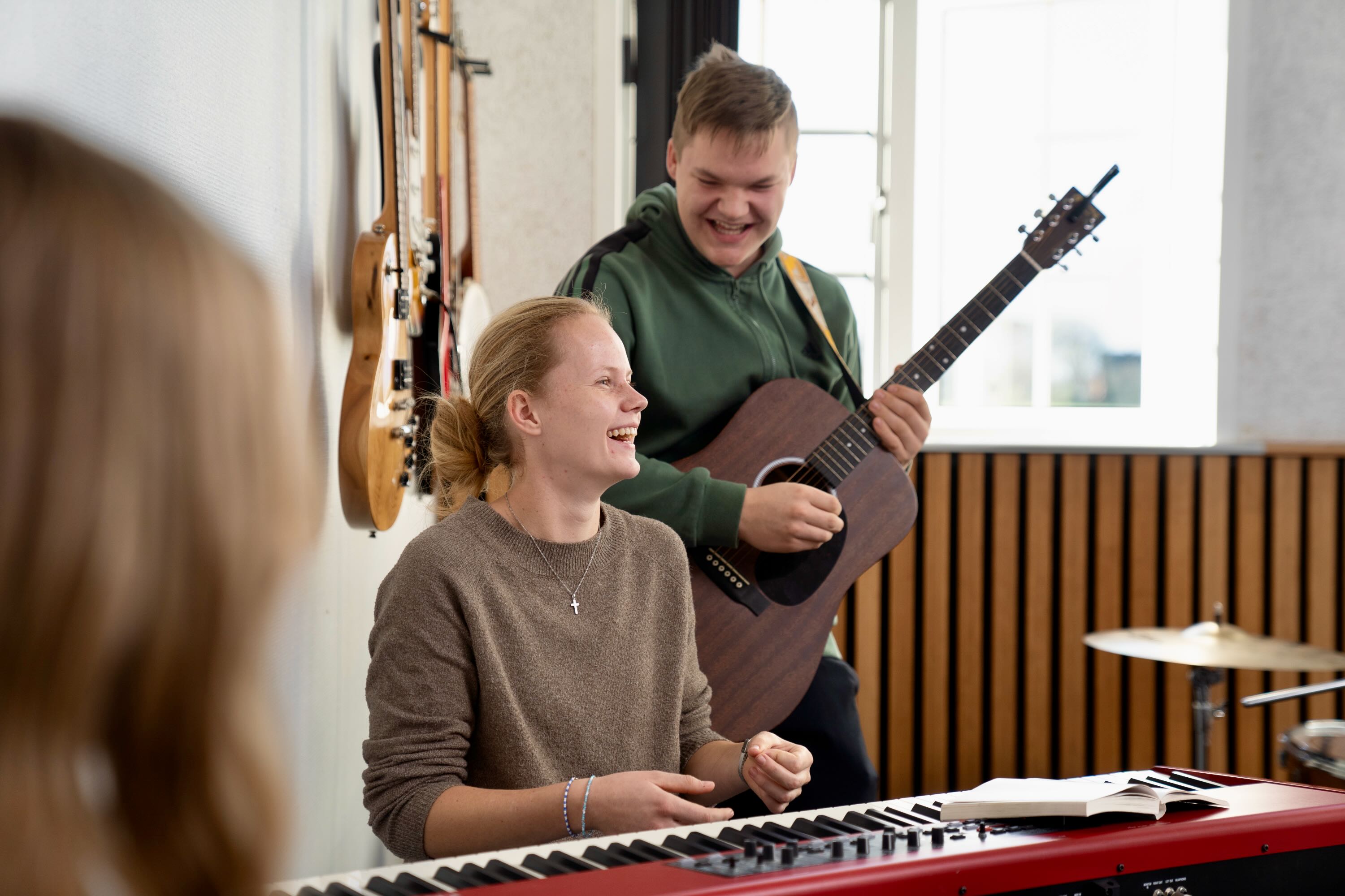 Musik Sædding Efterskole | To elever spiller i musiklokalet på Sædding Efterskole på henholdsvis klaver og guitar