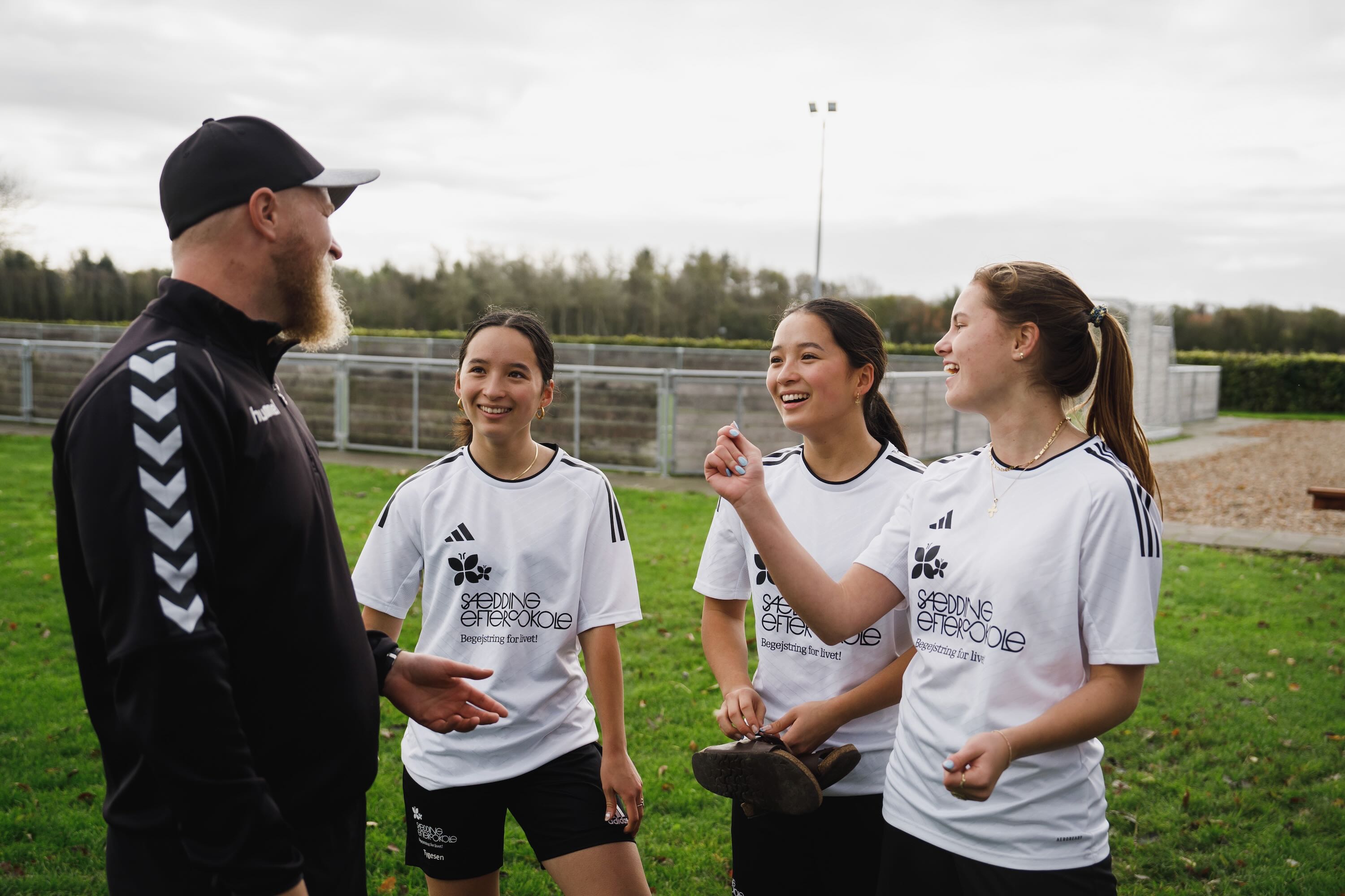 Lærerne på Sædding Efterskole | 3 piger i sportstøj snakker med en lærer på fodboldbanen
