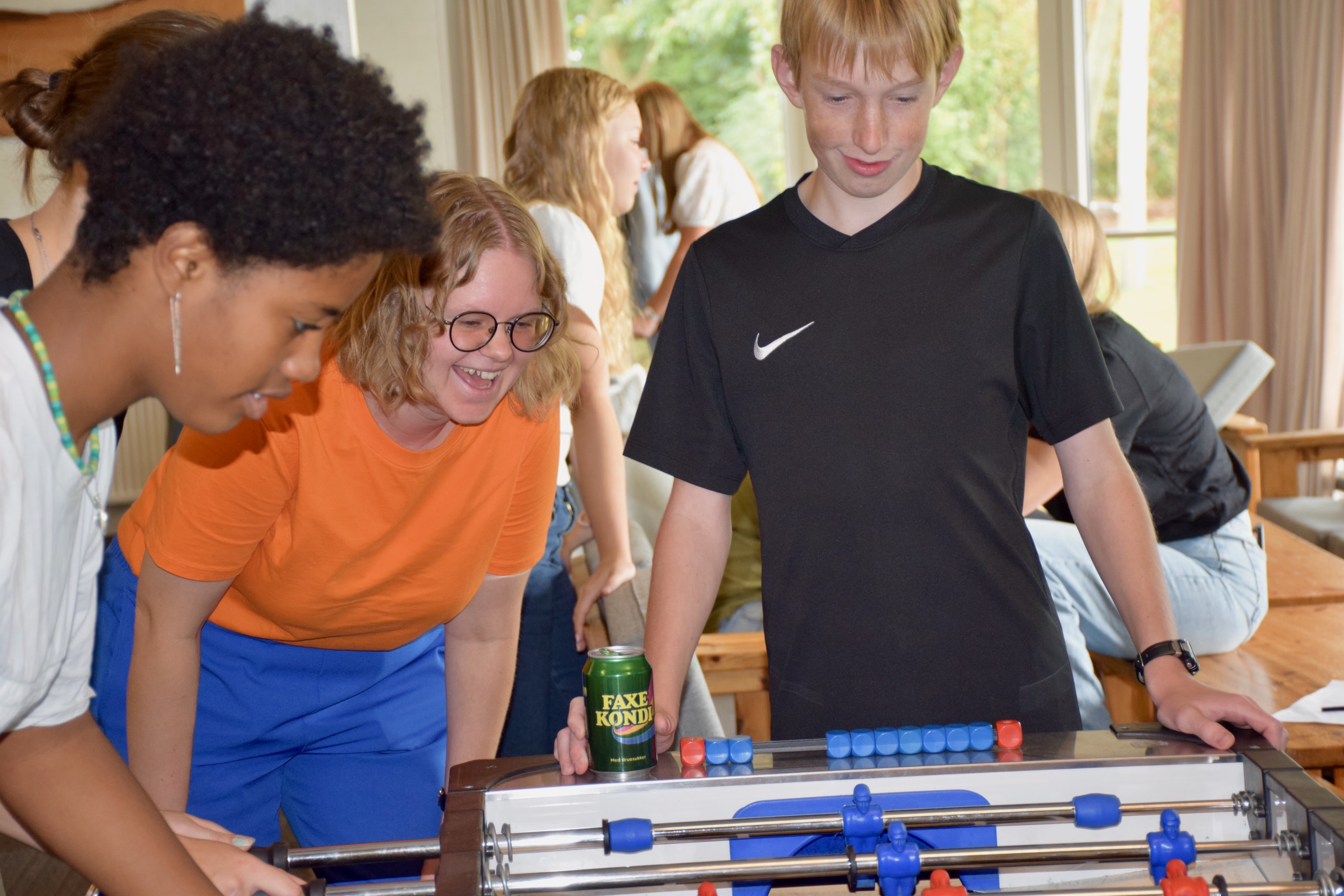 Inklusion Sædding Efterskole | En lærer og to efterskoleelever står i dagligstuen på Sædding Efterskole og spiller bordfodbold. Læreren griner ret meget. 