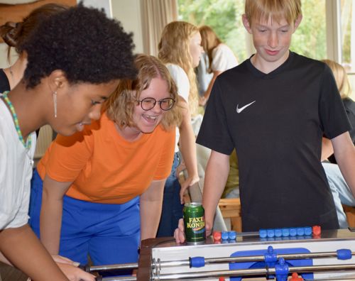 En lærer og to efterskoleelever står i dagligstuen på Sædding Efterskole og spiller bordfodbold. Læreren griner ret meget.