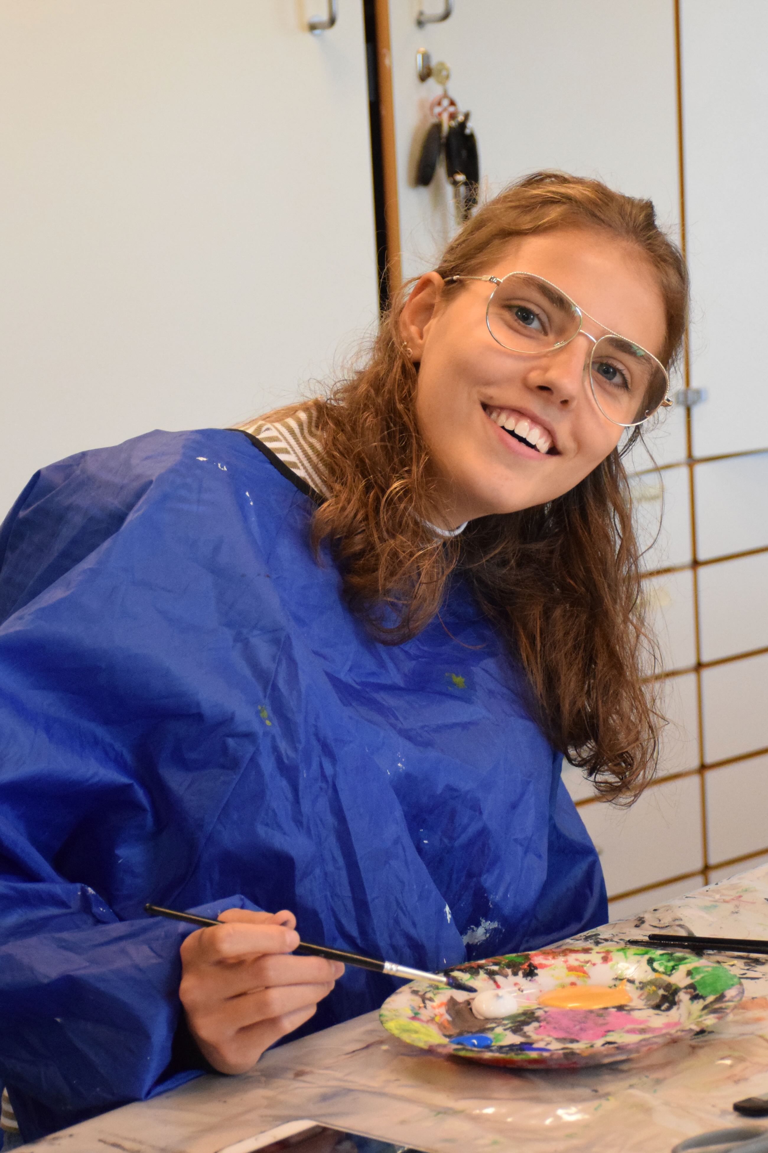 Kreativ Sædding Efterskole | Pige sidder med pensel og forskellige farver foran sig. Hun er klar til at male et maleri i krea.