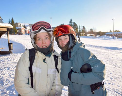 To piger står på en skibakke. Skibrillerne sidder i panden og de smiler.