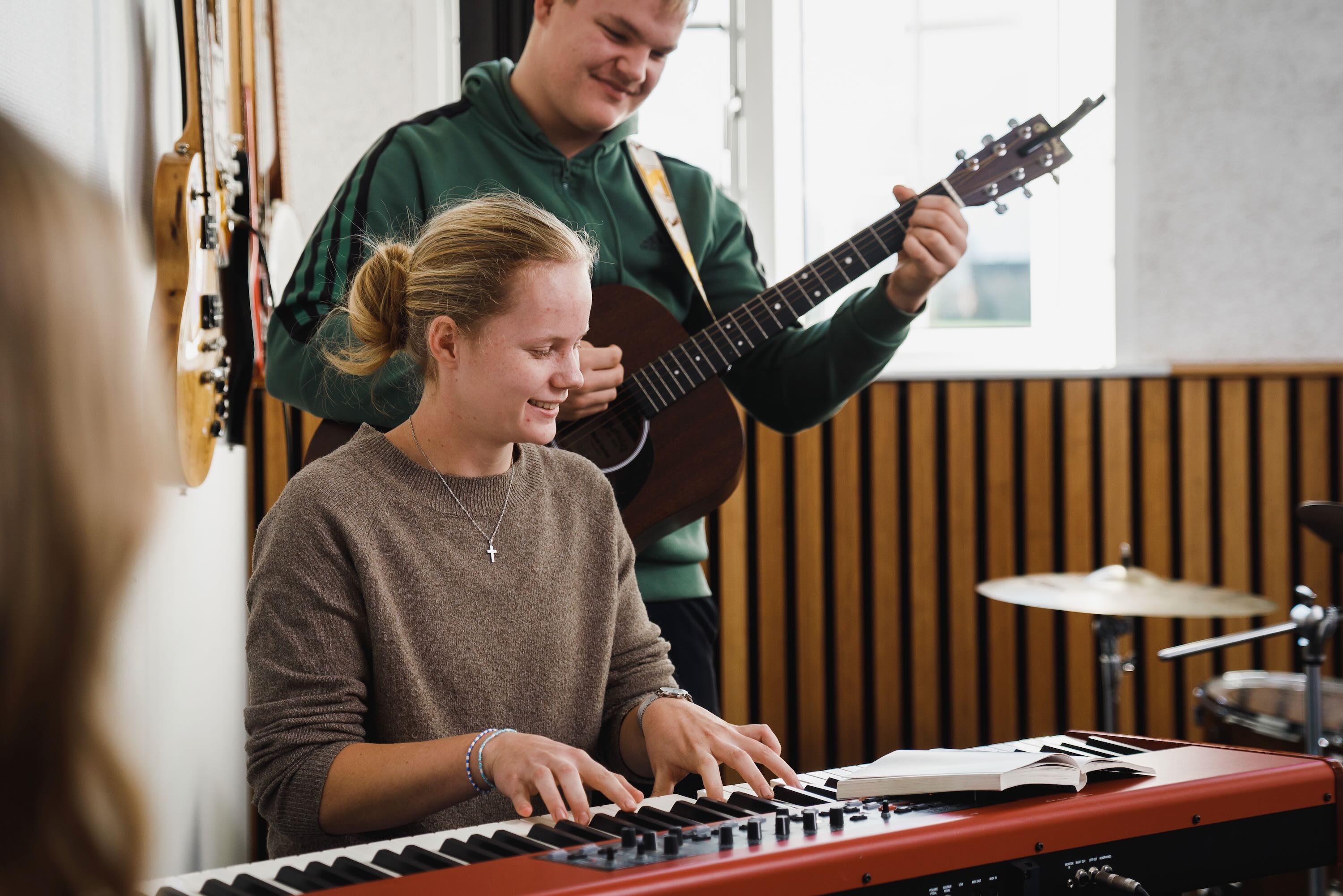 En efterskolepige spille klaver mens en dreng spiller guitar til i musiklokalet på Sædding Efterskole 